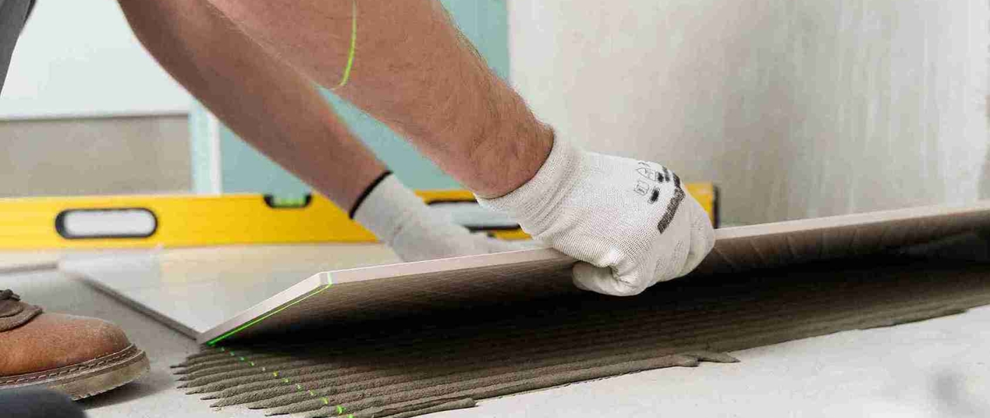 Tiler applying floor tiles using German polymer-based tile adhesive for strong and durable bonding