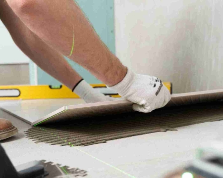 Tiler applying floor tiles using German polymer-based tile adhesive for strong and durable bonding