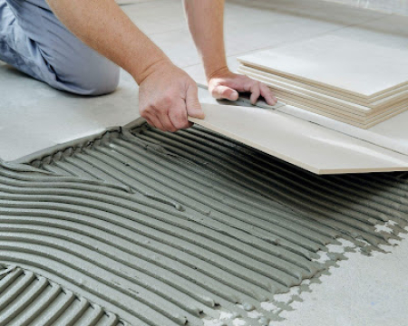 Professional applying VURA tile adhesive before installing ceramic floor tiles.