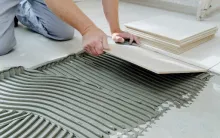Professional applying VURA tile adhesive before installing ceramic floor tiles.